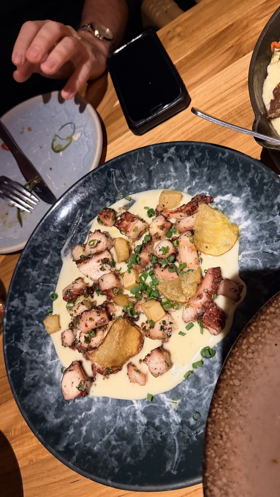 Pulpo a la brasa at Cantina del Tigre: charred pieces of octopus over a pale cream sauce with potato cubes, thin crisps and chives on a blue marbled plate