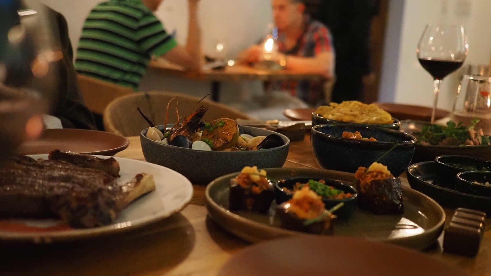 The cowboy ribeye at Kaandela on the table with the seafood casserole, pork belly pops and a glass of red wine