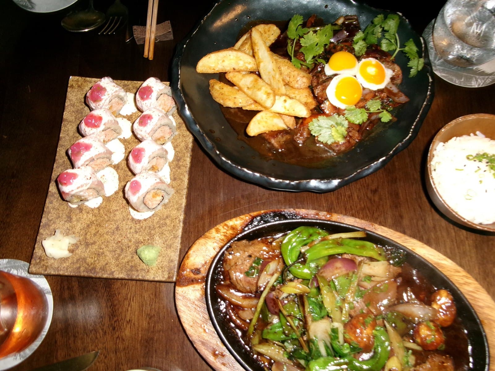 The table at Mai Mai an hour in: a roll topped with seared tuna, the lomo saltado, a bowl of rice and a sizzling pan of beef and peppers