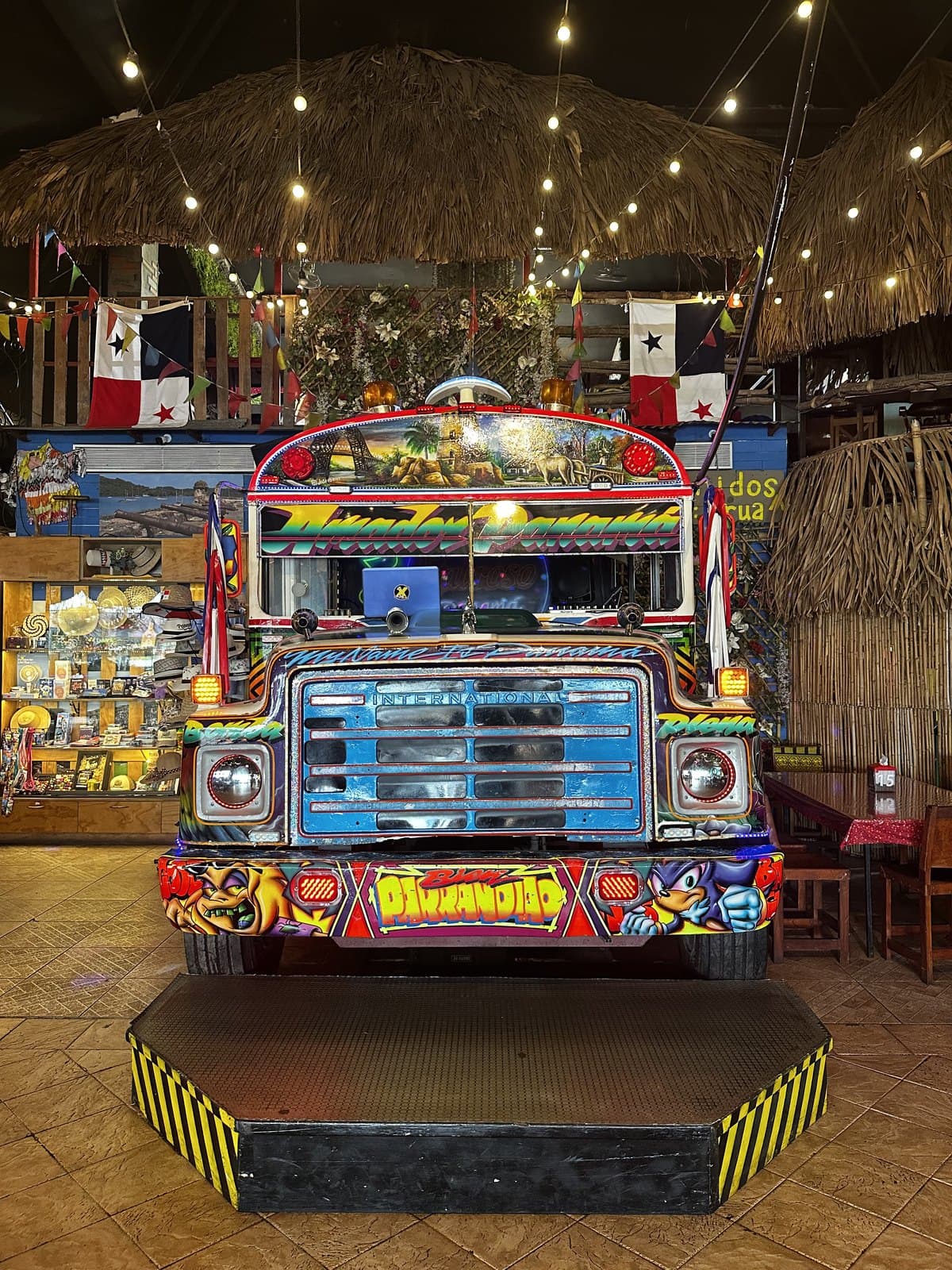 A painted Diablo Rojo bus installed inside Sabroso on the Amador causeway, under a thatched roof