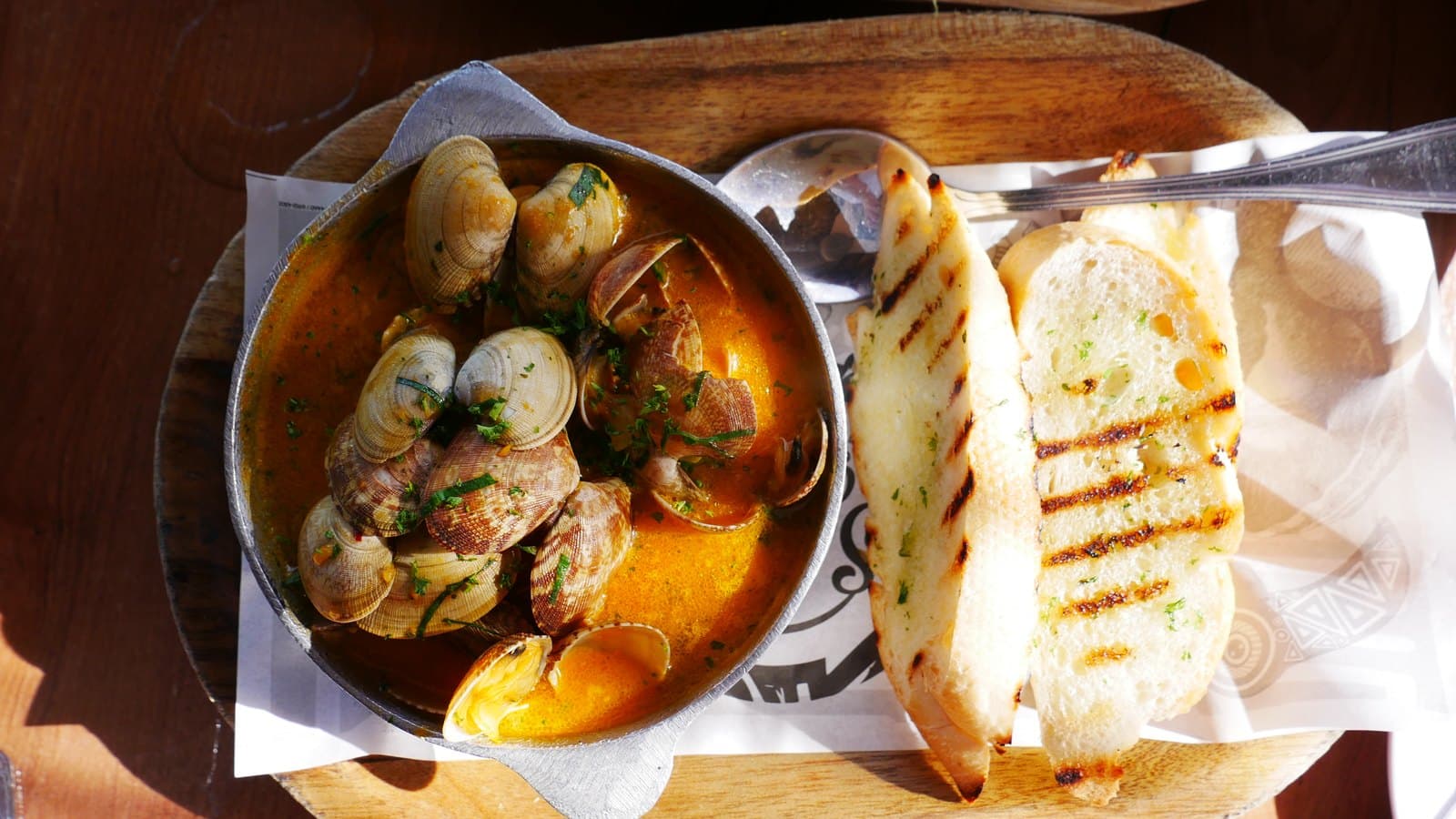 Garlic clams at Sabroso in a metal dish with grilled bread alongside