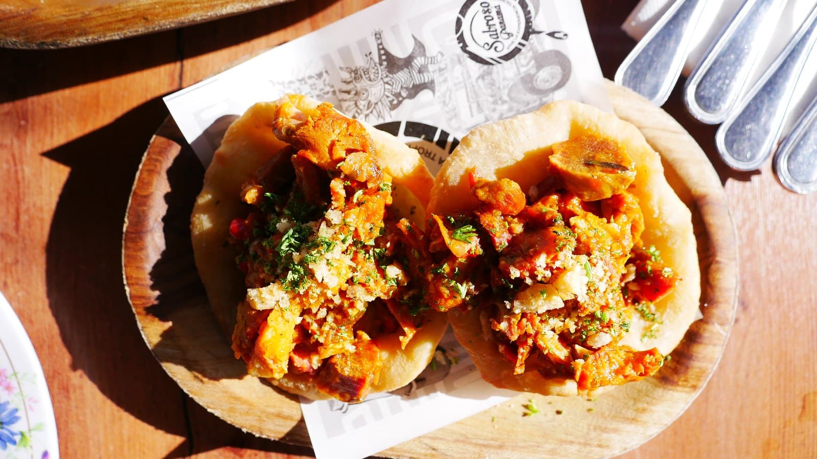 Fried dough rounds topped with shredded pork and sauce on a wooden board at Sabroso