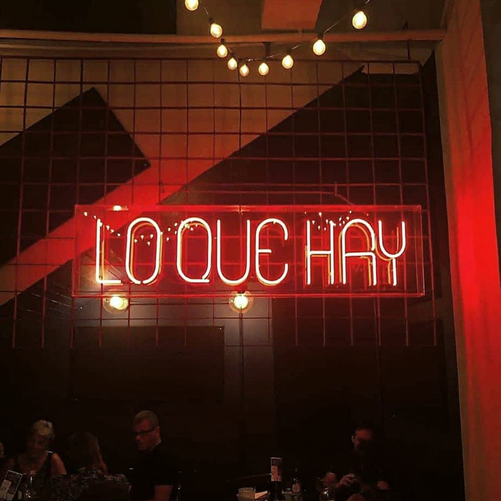 Interior dining room with a bookshelf wall and the “Lo Que Hay” neon sign at Fonda Lo Que Hay, Casco Viejo, Panama City