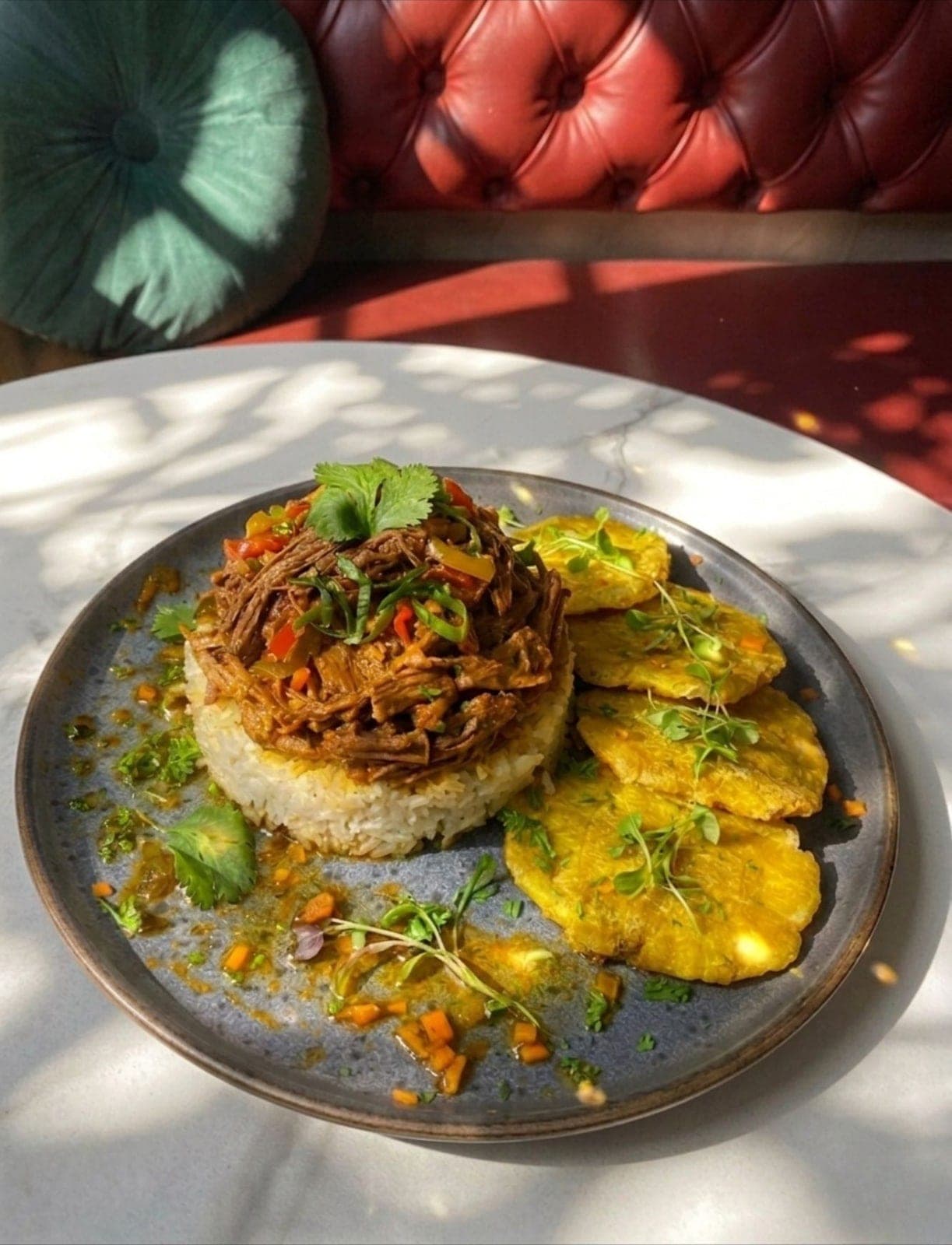 Shredded beef over rice with patacones and the red tufted banquette behind at La Divina Comida, Casco Viejo, Panama City
