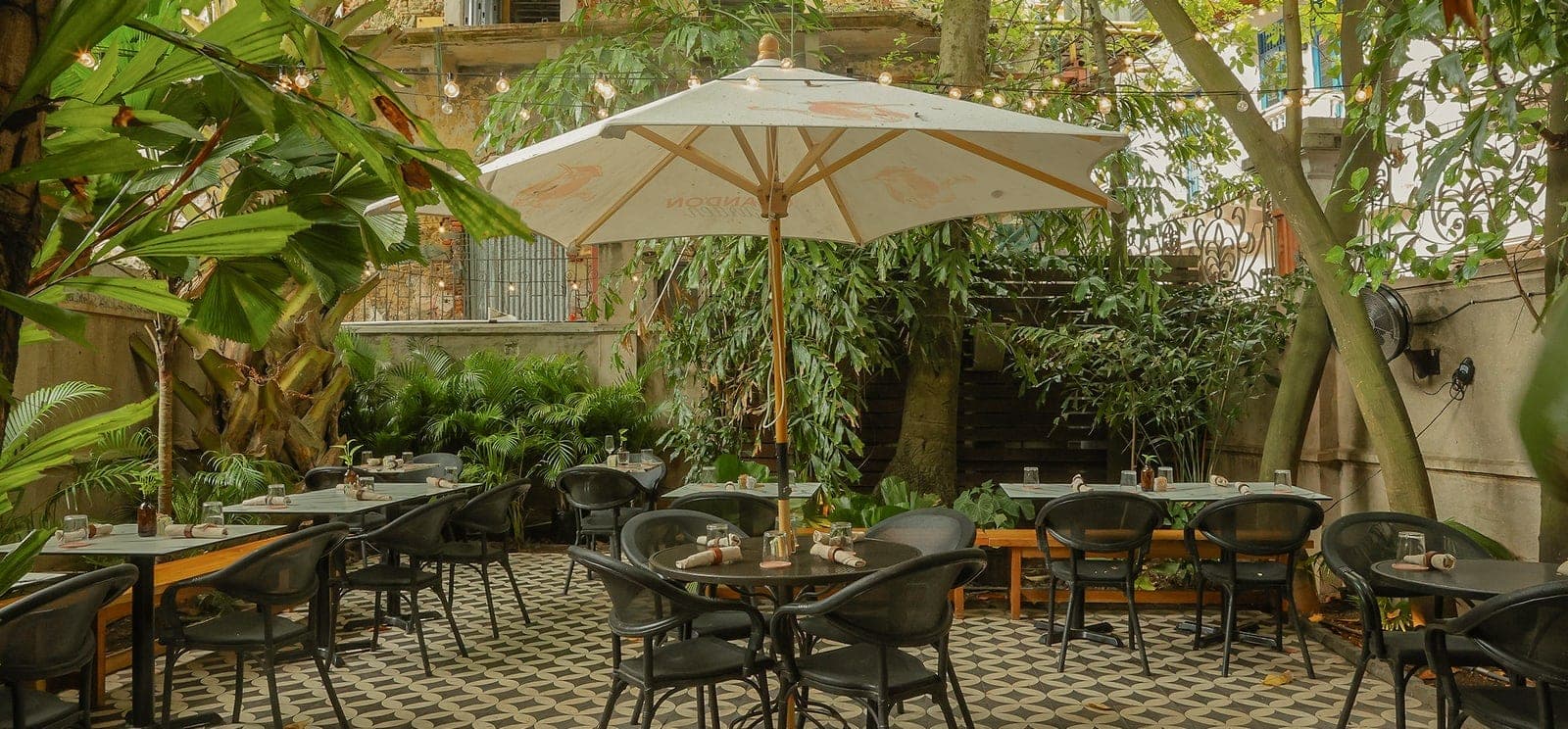 Lush garden patio with tables under an umbrella and string lights at Mahalo Cocina y Jardin, Casco Viejo, Panama City