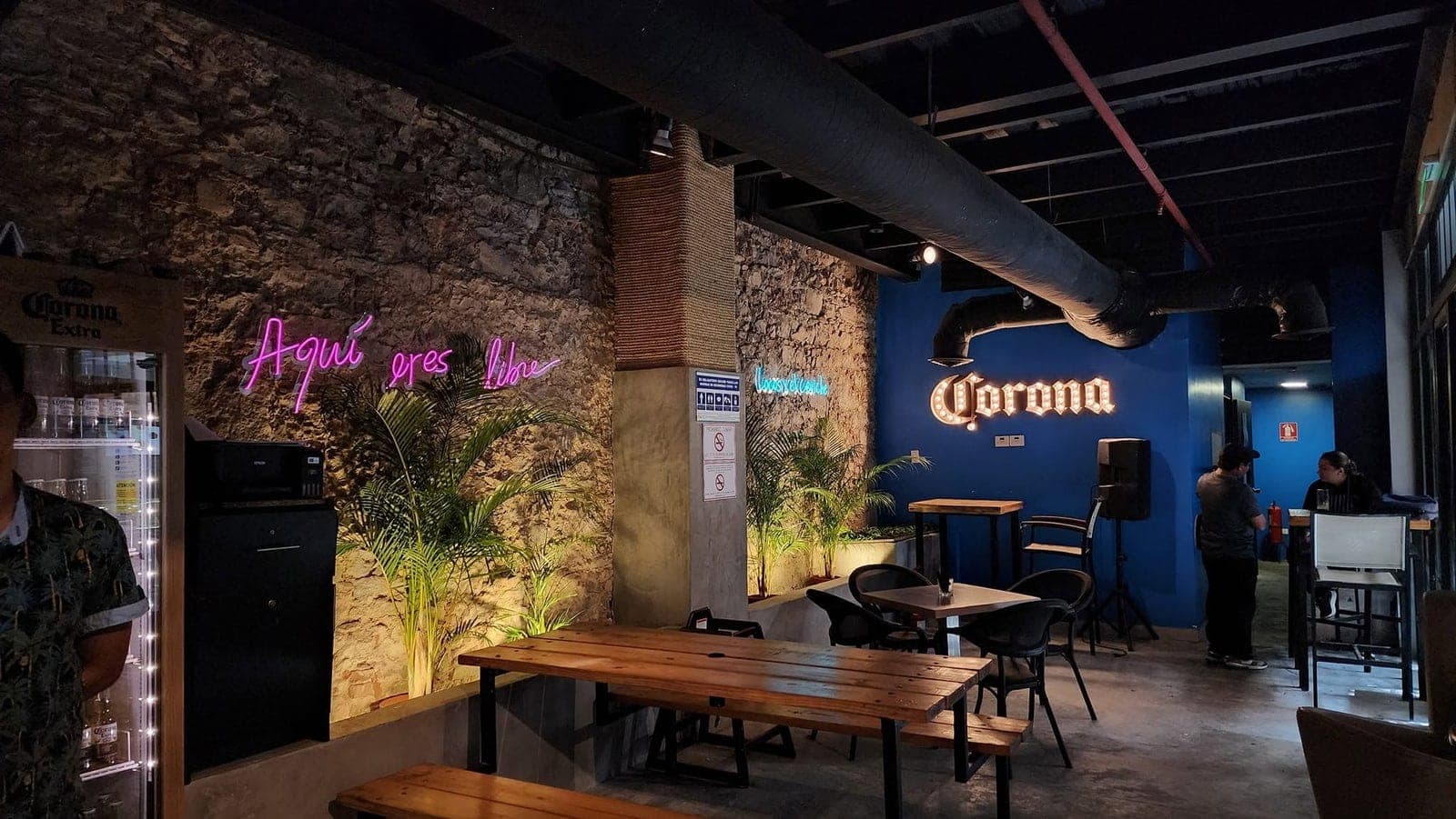 Interior con pared de piedra, letrero de neón y mesas comunales en Marea Casco, Casco Viejo, Ciudad de Panamá