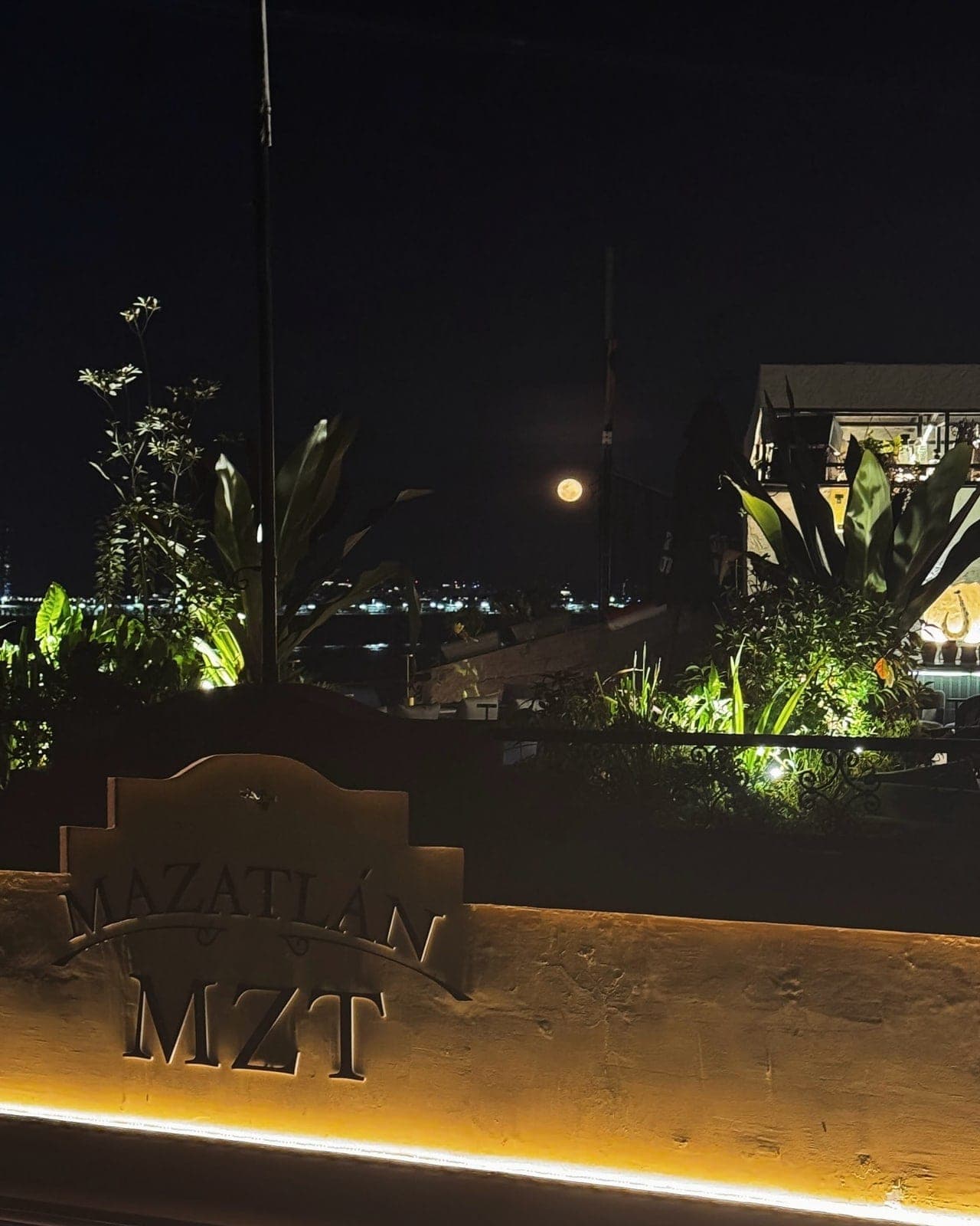 Terraza rooftop de noche con letrero del local y las luces de la bahía en Mazatlan Rooftop, Casco Viejo